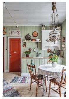 a dining room with green walls and wooden chairs in front of a red door that leads to the kitchen