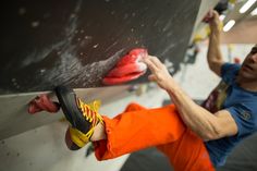 a man climbing up the side of a wall with his feet on a rope and wearing orange pants