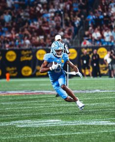 a football player running with the ball in his hand and people watching from the stands behind him