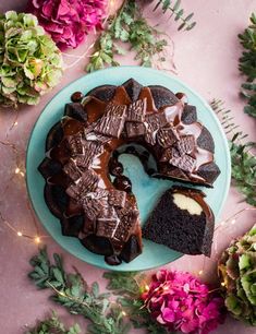 a chocolate bunt cake on a blue plate with one slice cut out and surrounded by greenery