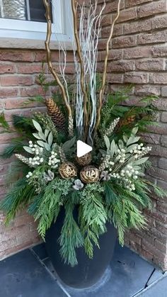 a potted plant with pine cones and greenery in front of a brick building