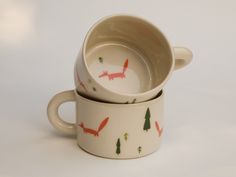 two mugs with foxes painted on them are stacked next to each other in front of a white background