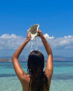 a woman standing in the ocean holding up a seashell over her head with water splashing from it