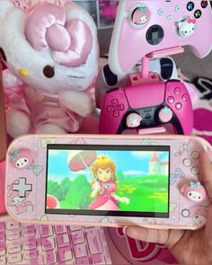 a person holding a pink nintendo wii game controller next to a stuffed animal and keyboard