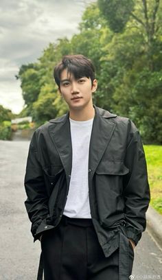 a young man standing on the side of a road wearing a black jacket and white t - shirt