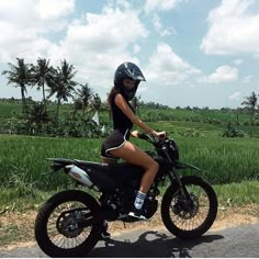 a woman riding on the back of a motorcycle down a road next to a lush green field