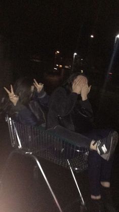 two people sitting in a shopping cart with their hands up to their face and one person covering their eyes