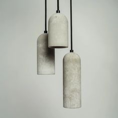 three cement lamps hanging from black cords in a room with white walls and flooring