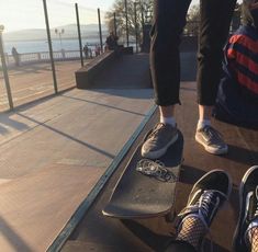 two people are standing on their skateboards at the top of a ramp near water