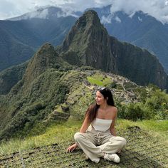 a woman sitting on top of a mountain next to a lush green valley with mountains in the background