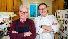 two men standing next to each other in a kitchen