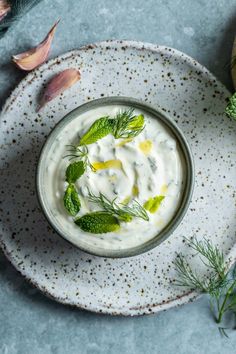 a bowl of yogurt with dill and herbs on a blue tablecloth