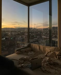 an unmade bed with a laptop on it in front of a window overlooking the city