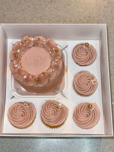 the cupcakes have pink frosting on them in a box with gold decorations