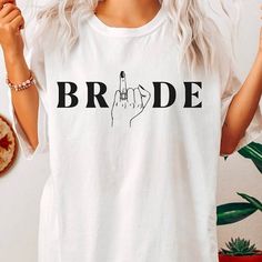 a woman wearing a t - shirt with the word bride written on it and a hand gesture