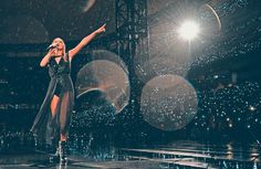 a woman standing on top of a stage with her arms in the air while singing