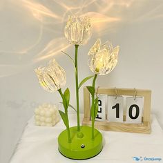 three flowers in a green vase next to a wooden frame with the number ten on it