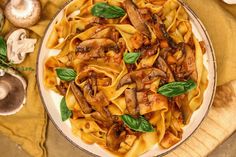 a plate of pasta with mushrooms and spinach on a yellow cloth next to some mushrooms