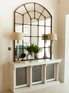 a mirror and some lamps on a table in a room with a window above it