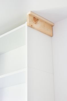 a white book shelf with wooden brackets on the top and bottom, against a white wall