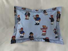 a blue and white striped pillow with baseball bears on it's sides, sitting on a bed