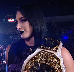 a woman with black makeup holding up a gold wrestling belt in front of a crowd