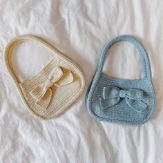 two crocheted purses sitting on top of a white bed next to each other