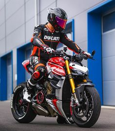 a man riding on the back of a red and white motorcycle next to a building