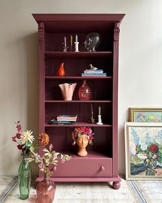 a purple bookcase with flowers and vases on top