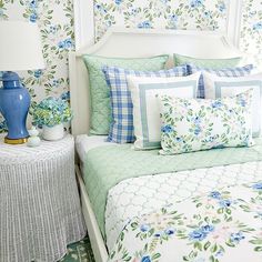 a white bed topped with lots of pillows next to a blue vase filled with flowers