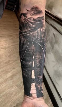 a man's arm with a train track and mountains on it