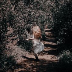 a woman is running down a path in the woods with her hair blowing back and she's wearing a white dress