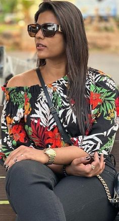 a woman sitting on top of a wooden bench wearing sunglasses and holding a purse in her hand