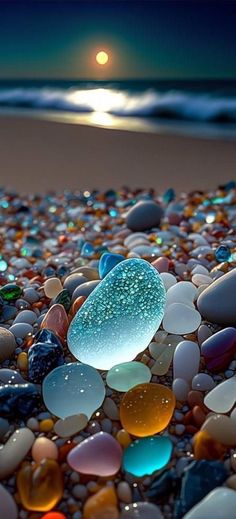 the beach is covered in many different colored rocks and pebbles at night, as the sun sets over the ocean