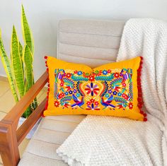 a yellow pillow sitting on top of a chair next to a potted plant