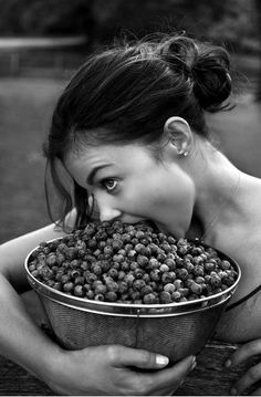 a woman is biting into a basket full of raspberries in black and white