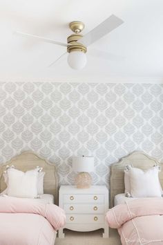 two twin beds with pink comforters and white nightstands in front of patterned wallpaper