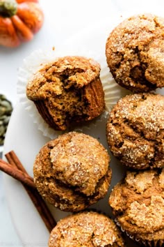 several muffins on a plate with cinnamon sticks and pumpkins in the background