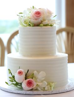 a three tiered white cake with pink and white flowers on the top, sitting on a table