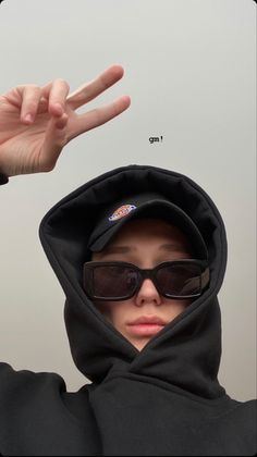 a person wearing sunglasses and a hoodie making the peace sign with their fingers in front of them