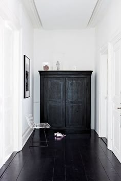 a black cabinet sitting in the middle of a hallway next to a white wall and wooden floor