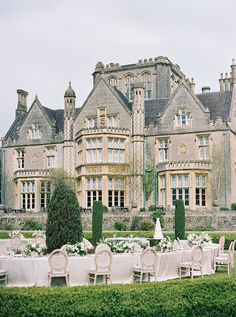 an outdoor dining area with tables and chairs in front of a large stone building surrounded by greenery