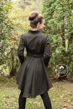 a woman standing in the grass with her back to the camera, wearing a black coat and leggings