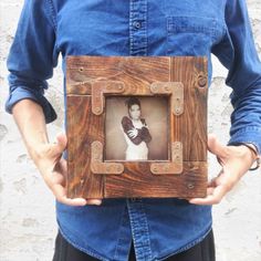 a man holding up a wooden frame with a photo in it's center and his hands behind him