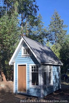 a small blue shed with a brown door and windows on the side, in front of some trees