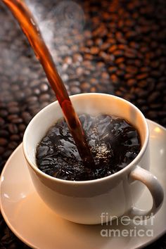 a coffee cup filled with liquid sitting on top of a saucer next to beans