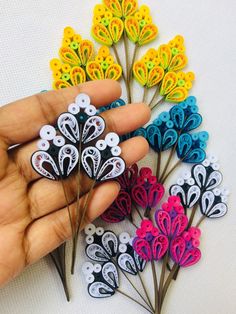 a hand is holding several small flowers made out of paper and thread on a white surface