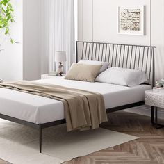 a bed with white sheets and pillows in a room next to a plant on the floor