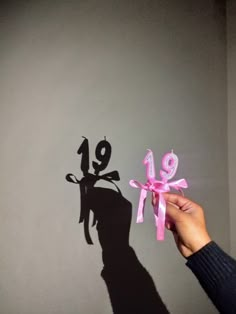 the shadow of a person's hand holding a pink ribbon in front of a gray wall