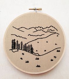 an embroidered wall hanging with trees and mountains in the background, on a white surface